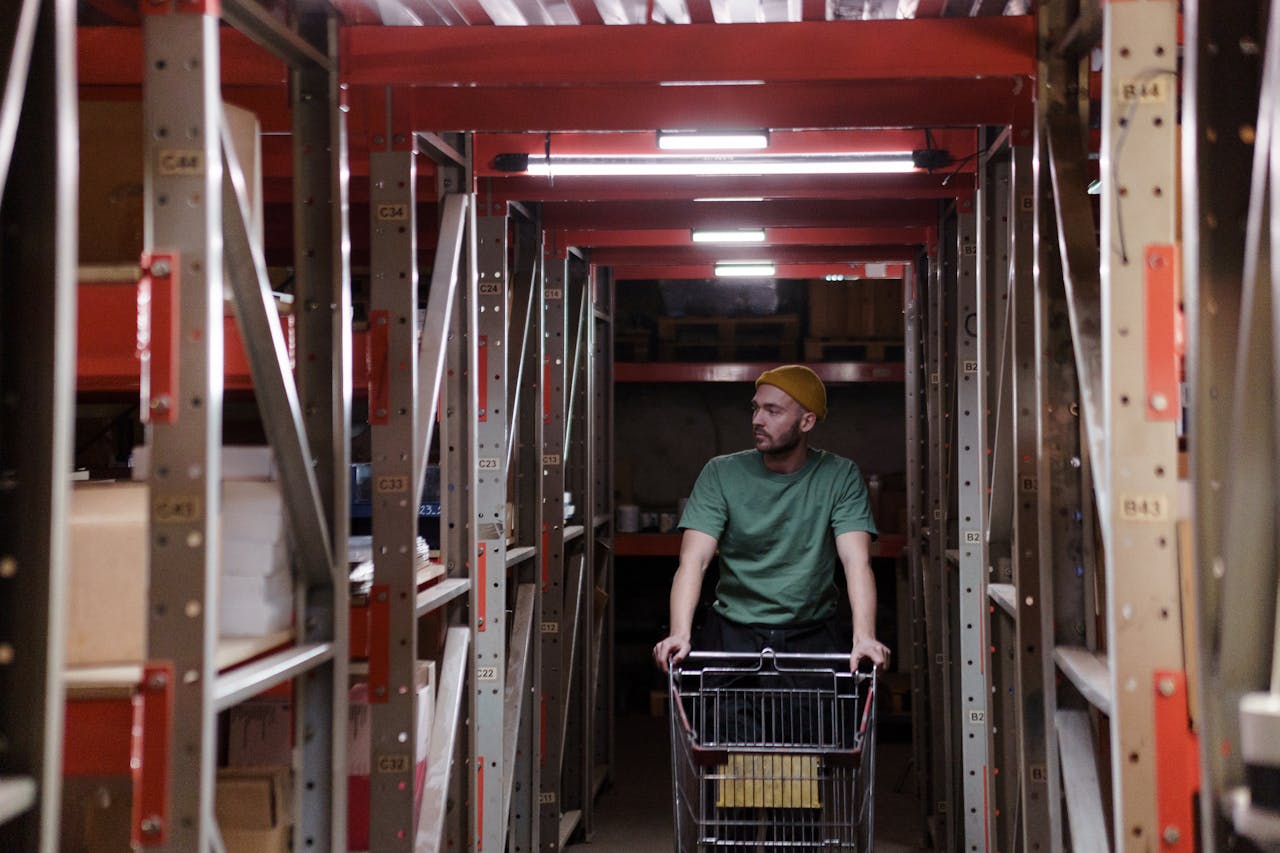 A worker in a warehouse pushing a cart through shelves, depicting concentration and industrial work.